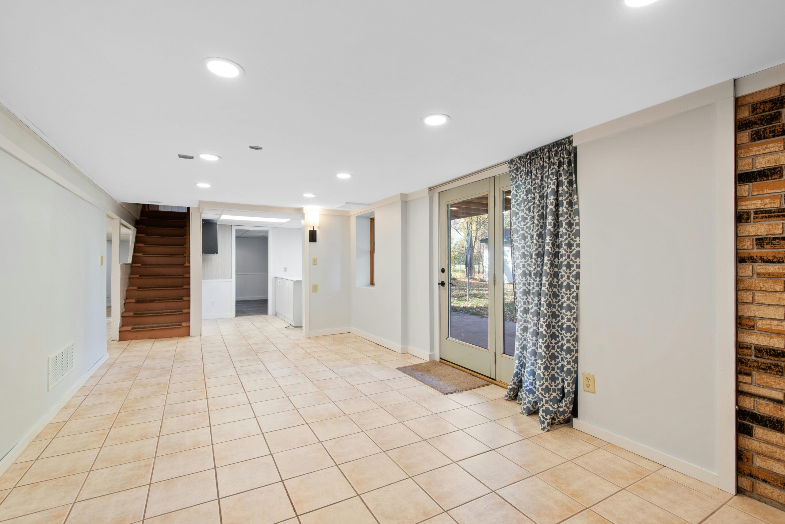 Open-concept basement with tile flooring, bright lighting, and outdoor access for added living space in Midland