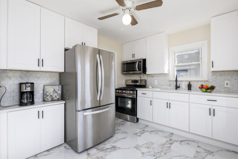 Modern kitchen remodel in Warren, MI by Remodeling Warriors featuring stainless steel appliances, white shaker cabinets, and marble-look tile flooring.